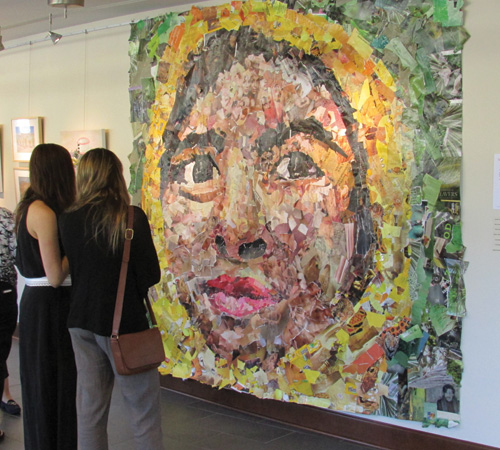 Two women observing a wall-sized mural of a face, made up of colorful decoupage
