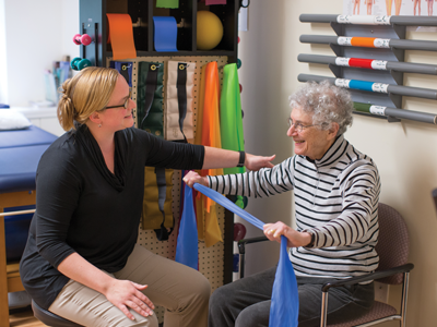 A female physical therapist working with a senior woman who is holding up a blue scarf