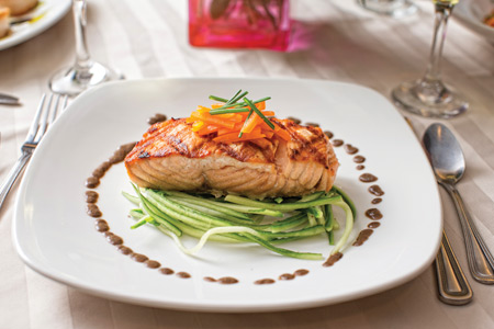 A white dinner plate with a salmon steak, garnished with carrots and greens