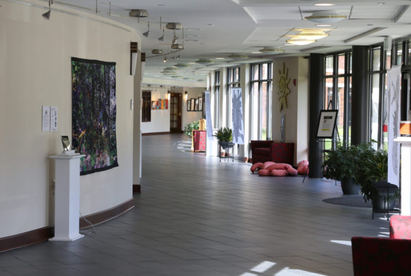 A hallway at Whitney Center, with works of art displayed on the walls, easels and pedestals