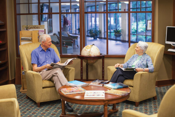 A smiling senior man and woman sitting in armchairs have a conversation in one of Whitney Center's common rooms