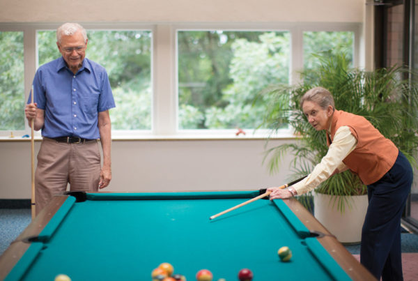 A senior couple playing billiards in a Whitney Center common room