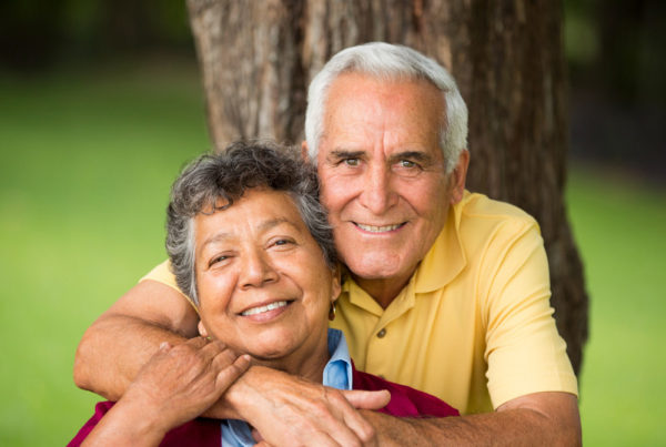A senior couple smile and pose in front of a tree