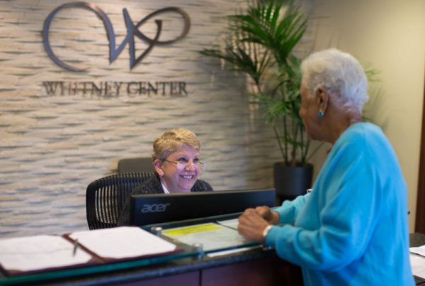 A staff member assists a resident at the front desk of Whitney Center